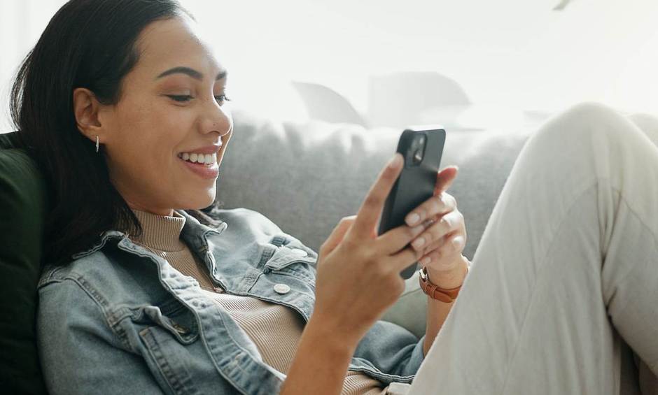 Frau liegt auf dem Sofa und hält ein Handy in der Hand.